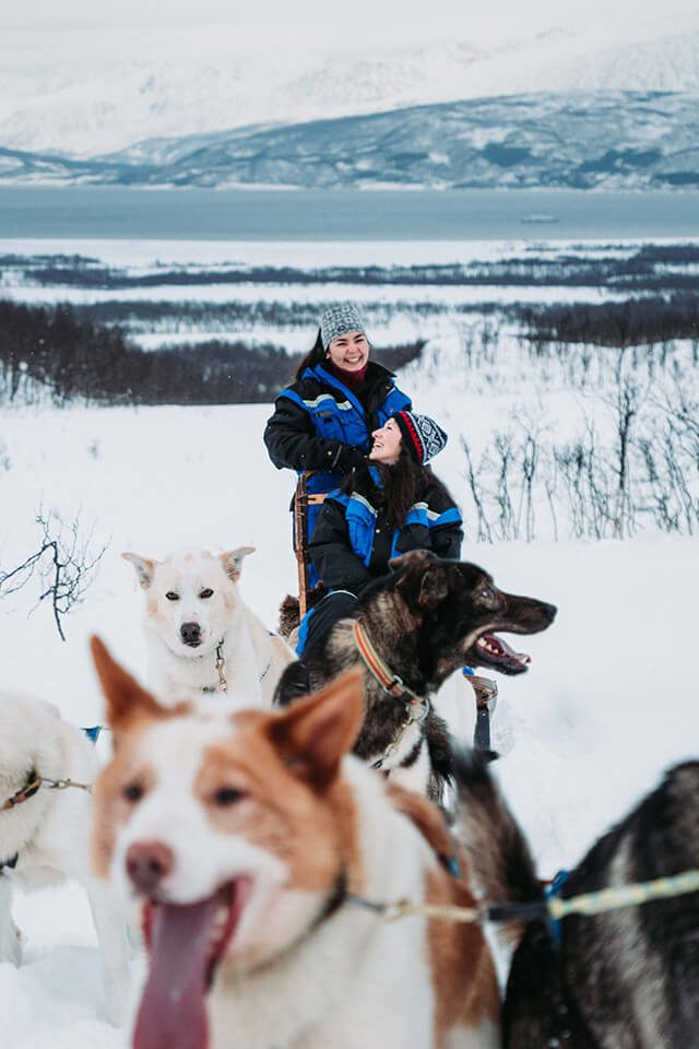 Two women dog sledding and smiling
