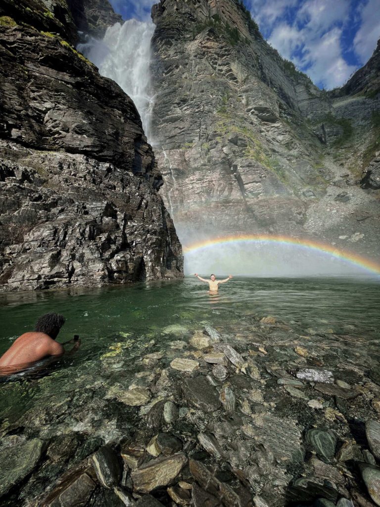 people bathing in stream with waterfall and rainbow
