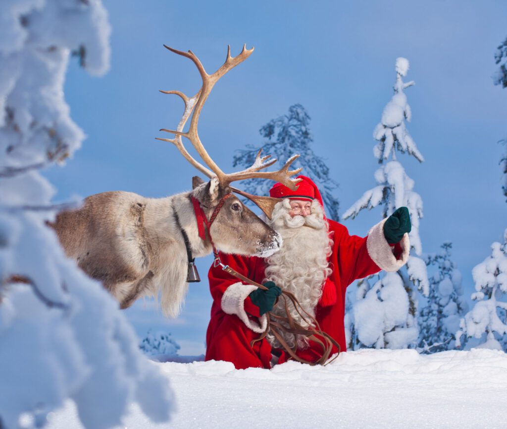 Santa Claus and a reindeer pointing towards a out of frame point with snow covered trees in the background