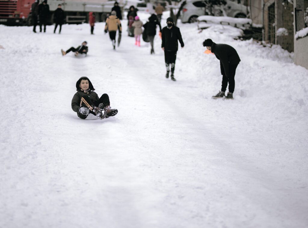 People and children going downhill on a plastic sleigh