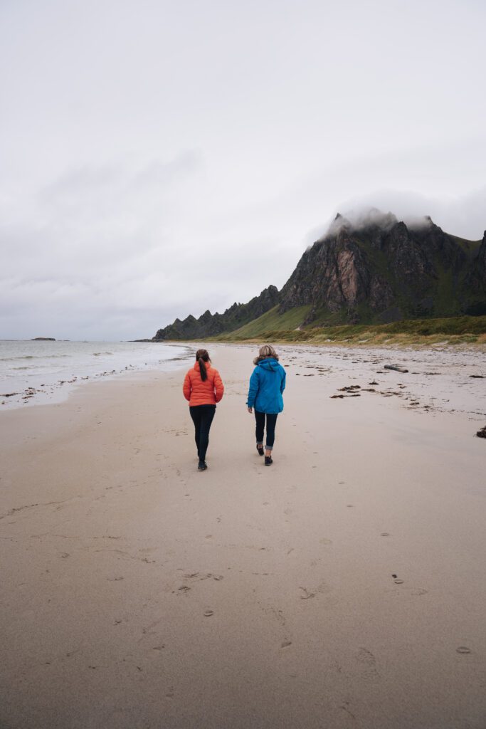 two people from the back on the beach looking towards a misty mountain