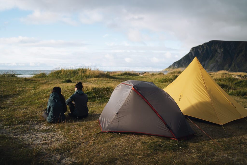 two people and two tents on a beach with mountain in the background