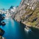 Boat cruising through a narrow fjord with steep mountains and clear blue water in Norway
