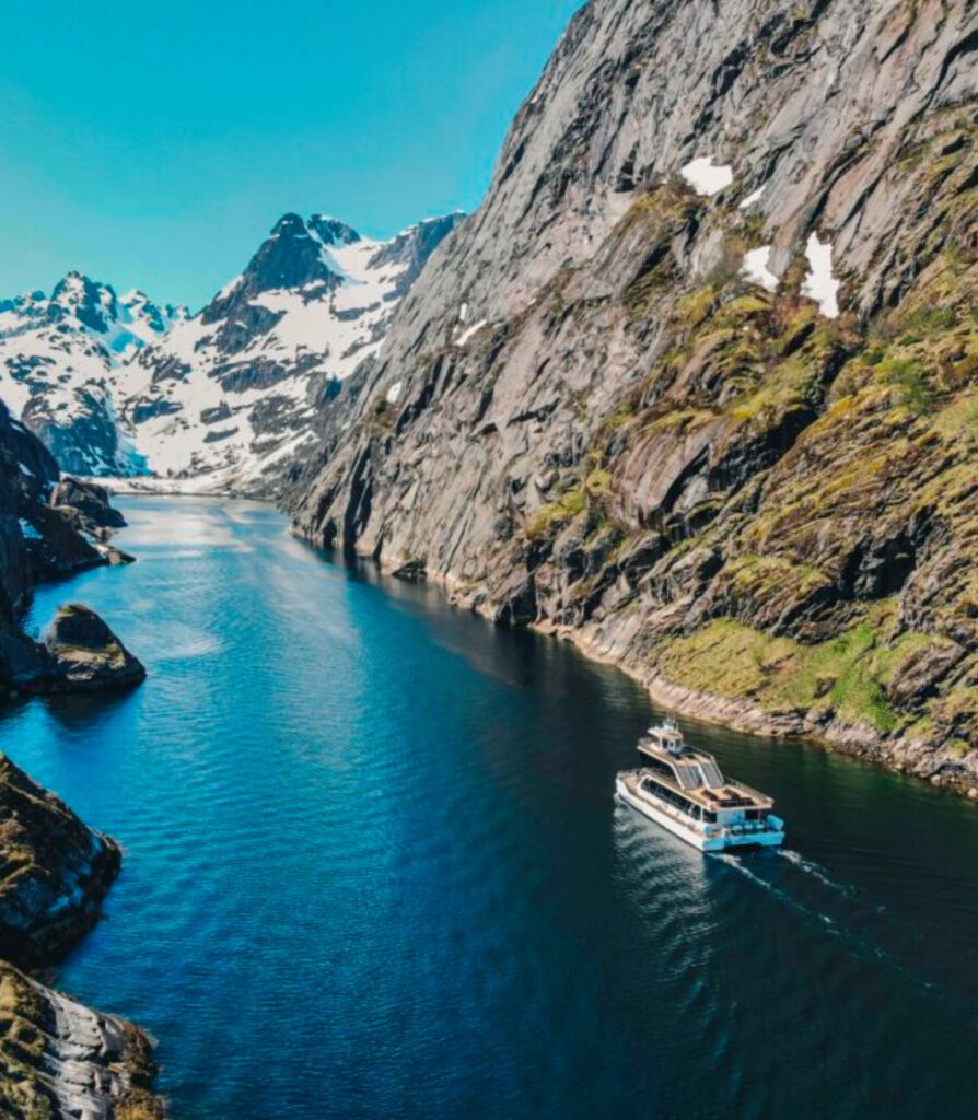 Boat cruising through a narrow fjord with steep mountains and clear blue water in Norway