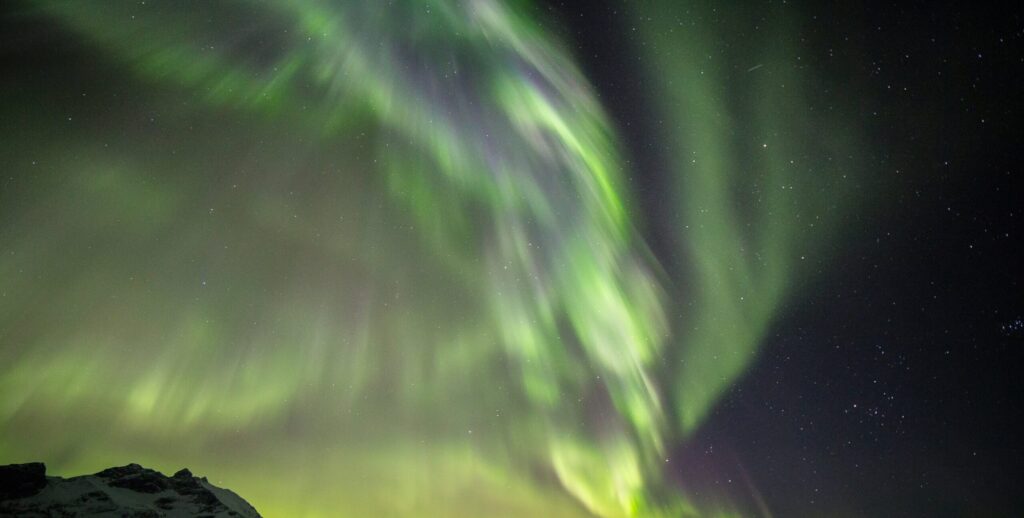 Green and purple northern lights glowing in a dark, starry night sky