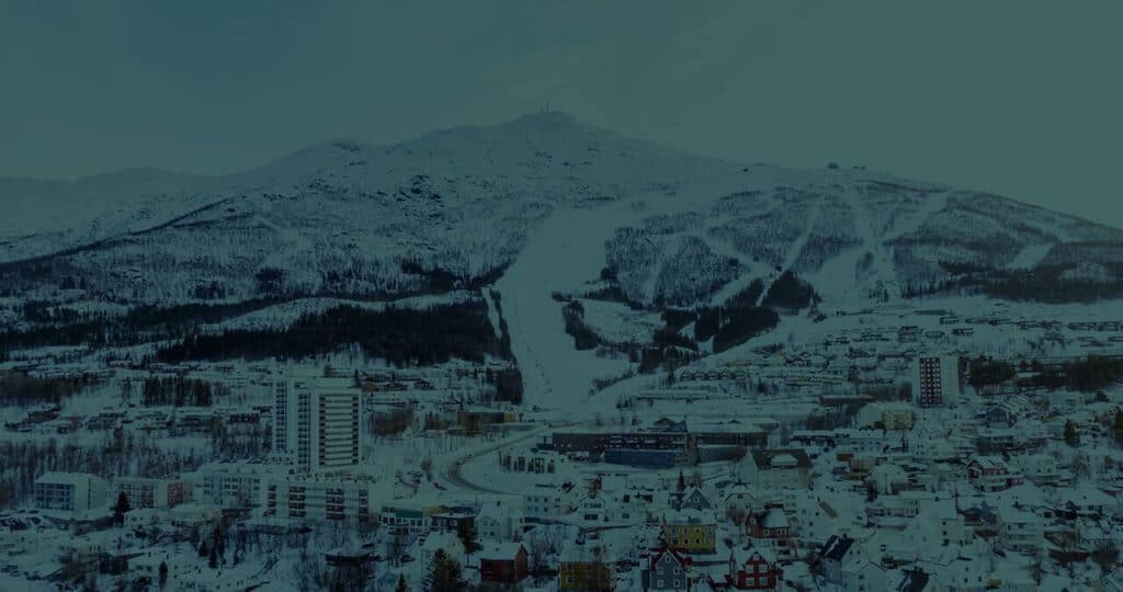 Village with colorful houses covered in snow and a snowy mountain in the background.