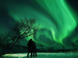 A couple watching the northern lights over snowy mountains at night