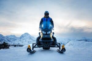 A person standing on a snowmobile in front of a breathtaking snowy landscape
