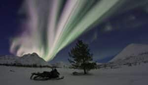 A snowmobile is parked on a snowy trail, with mountains in the background and under a pink sunset.