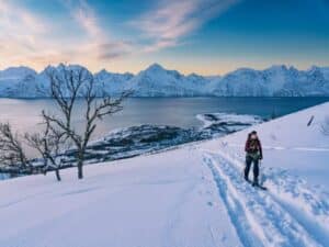 Woman cross-country skiing on a snowy mountain with fjord and snow-covered peaks at sunset