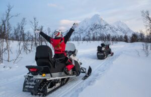 A person wearing thermal suit and helmet is enjoy a thrilling snowmobile tour through Lyngen Alps landscapes.