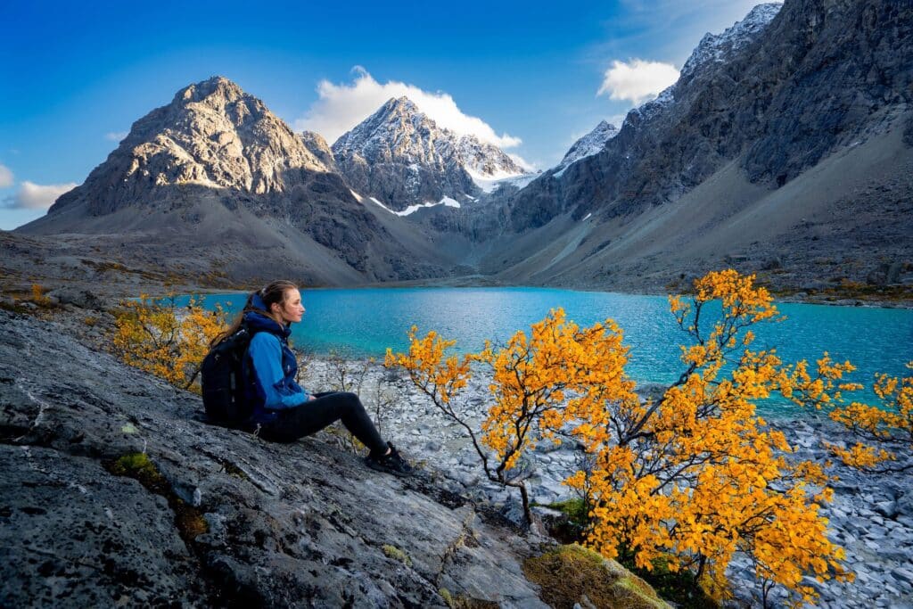 Person sitting on a rock overlooking the Lyngen Alps and blue fjord waters on a sunny summer day