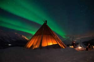 Green northern lights above a small hut in a winter landscape