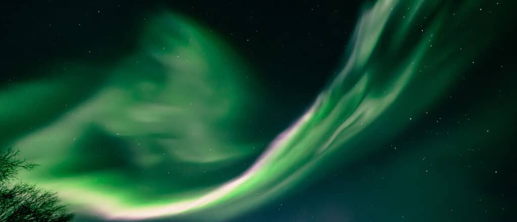 Flowing green northern lights stretching across a dark starry Arctic sky