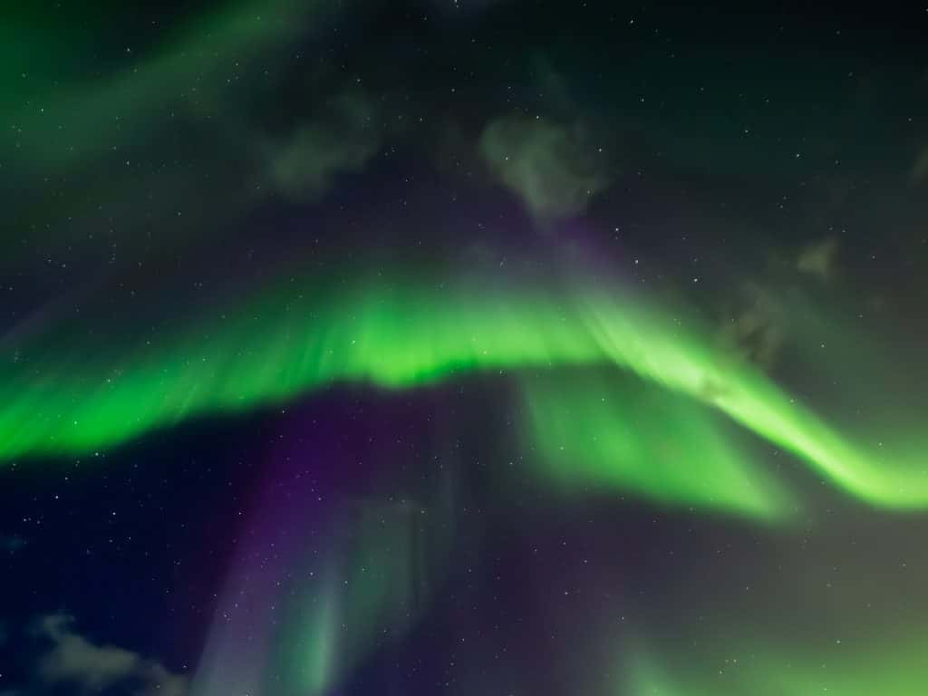 Green and purple aurora borealis in a dark blue arctic sky