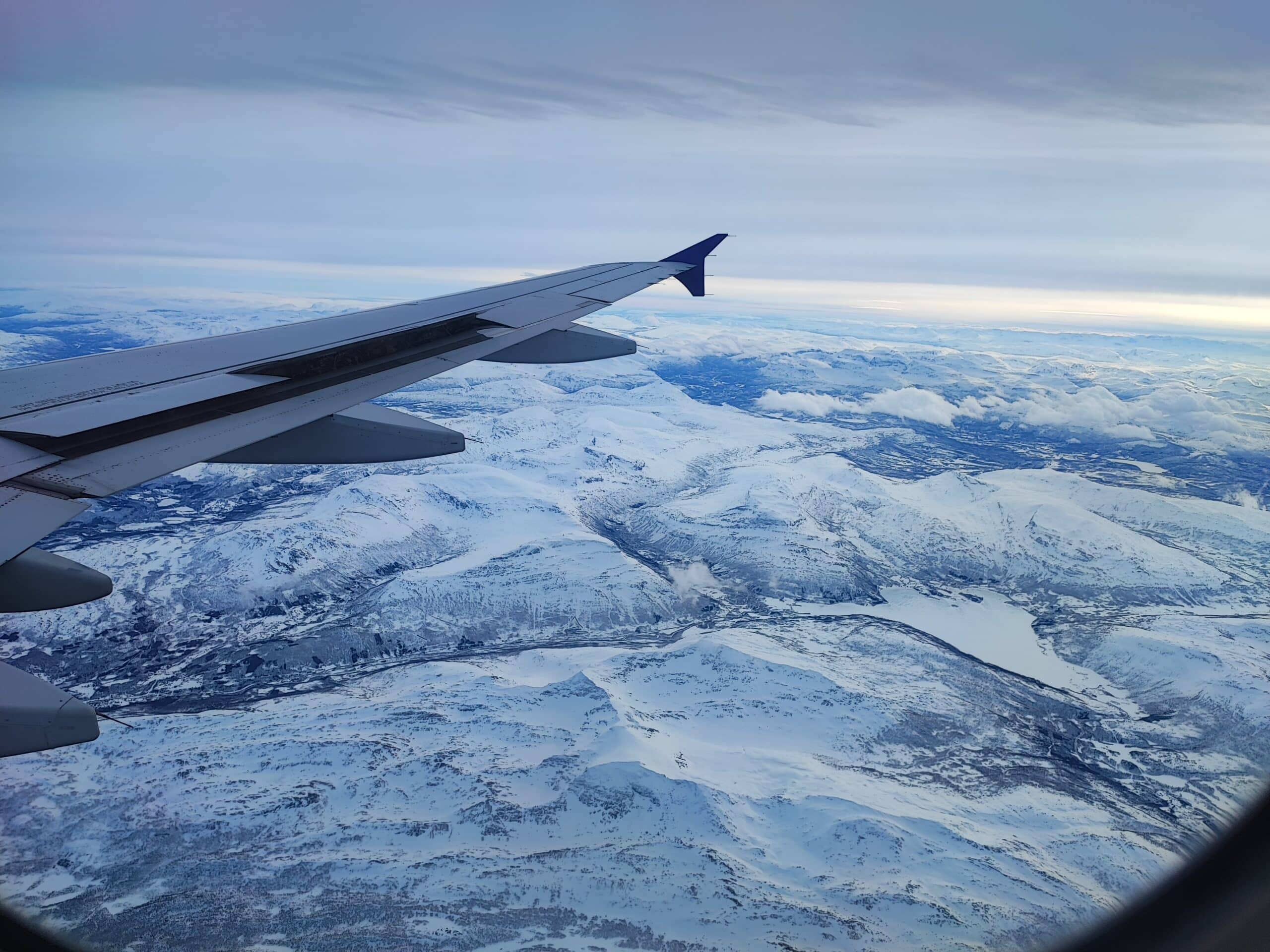 View from an airplane window showing the right wing above snowy mountains near Tromsø, Northern Norway