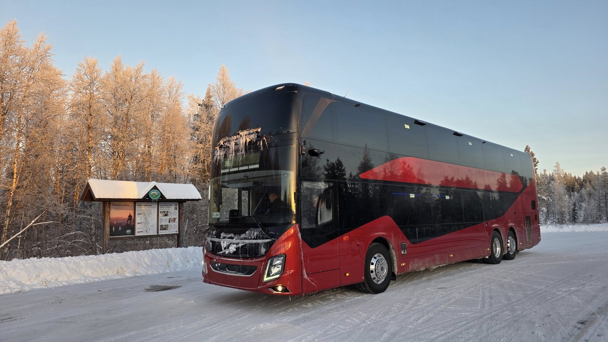 Aurora Express double-deck tour bus parked on a snowy roadside surrounded by winter forest between Tromsø and Rovaniemi