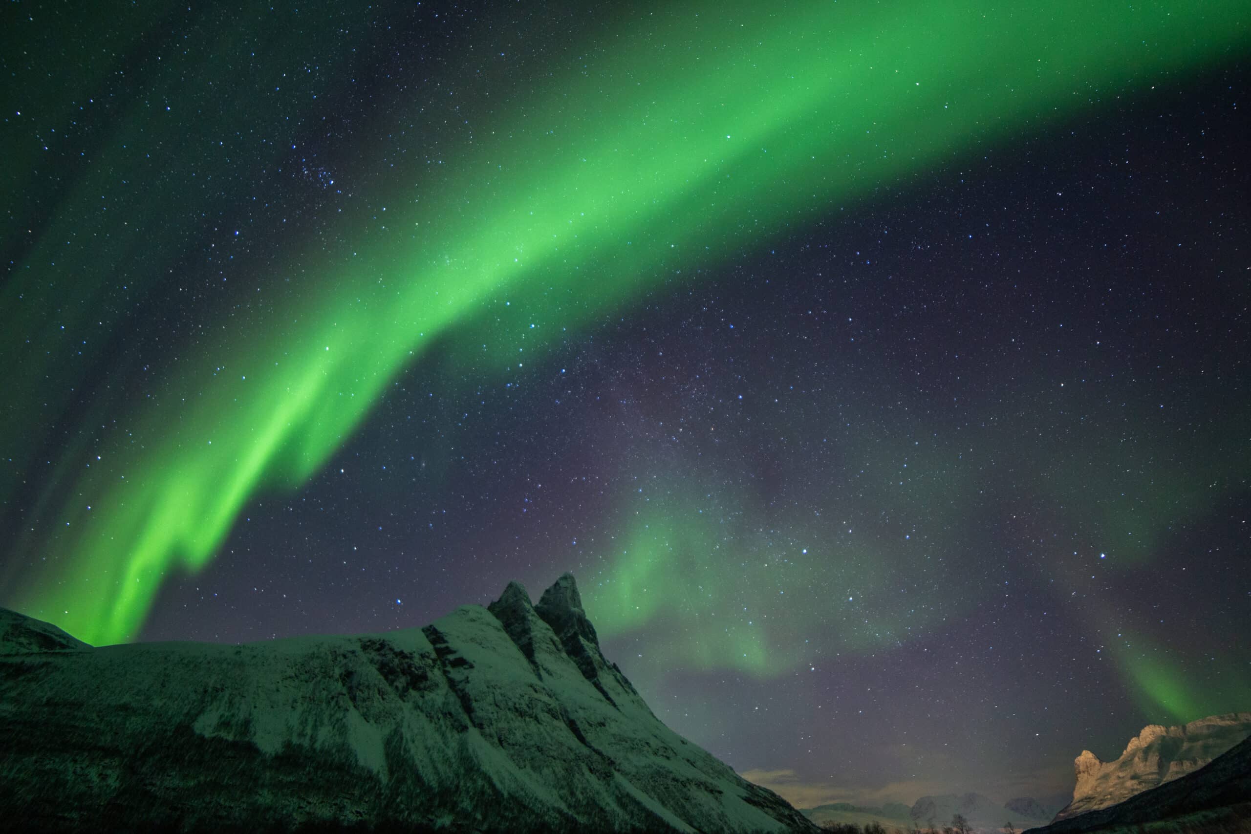 Snowy mountains in Tromsø region under green and purple Northern Lights in a starry Arctic sky