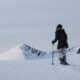 A woman participating in a guided snowshoe hike on a snowy mountain ridge in Kvaløya, Norway with alpine peaks in the background