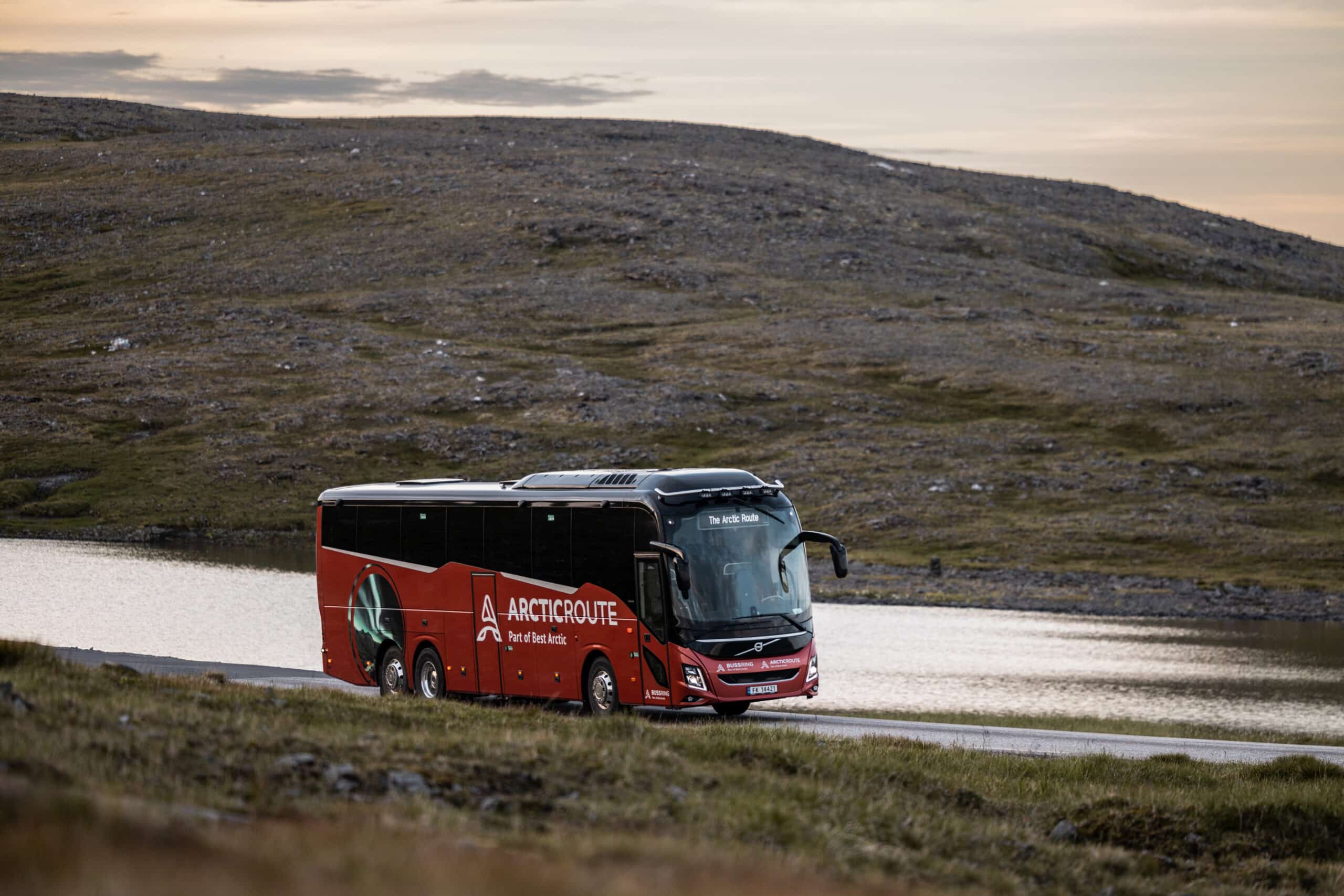 Red Arctic Route bus driving along a summer road in northern Norway