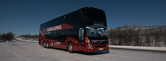 Aurora Express double-deck red bus from Best Arctic stopped on a snowy road under a starry night sky