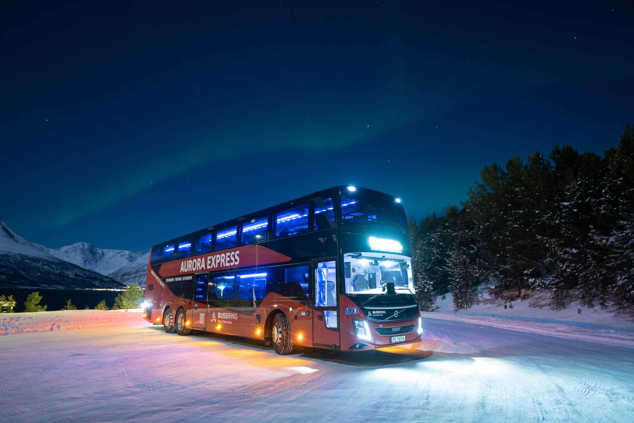 Aurora Express double-deck red bus from Best Arctic stopped on a snowy road at night under the northern lights