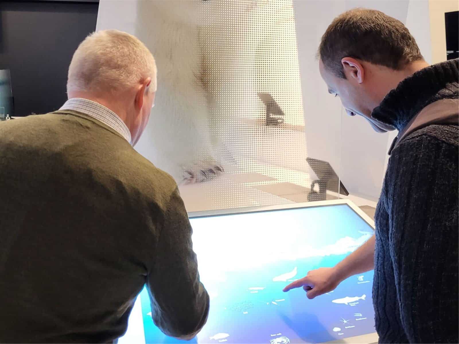 Two men stand in front of a screen showcasing different maritime species during a visit to Polaria.